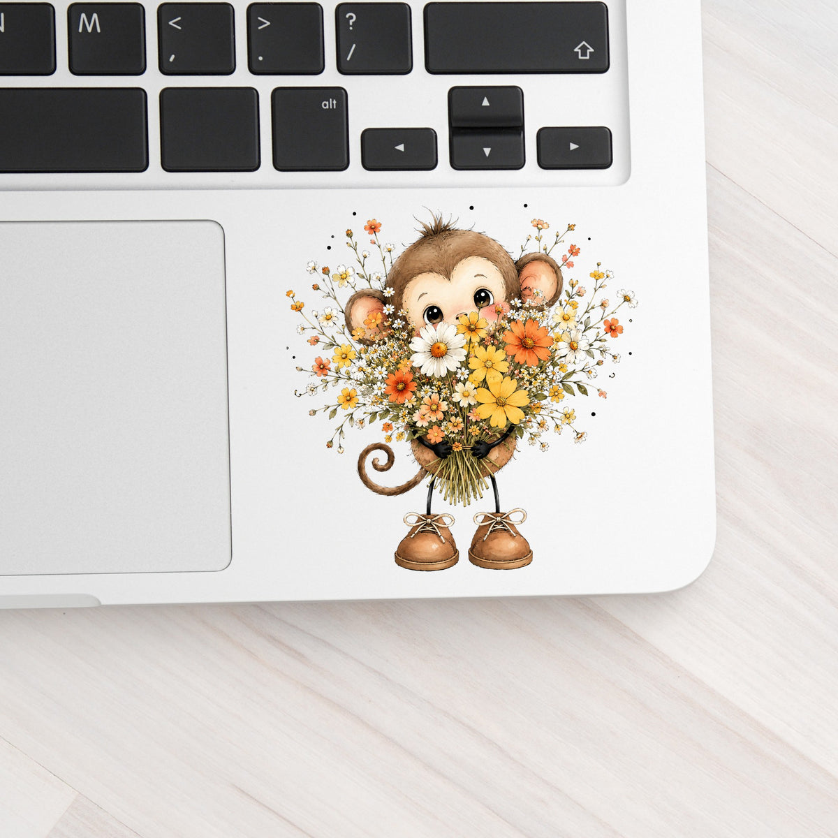 Baby Monkey Holding Daisy Bouquet UV DTF sticker applied to a silver laptop beside the keyboard