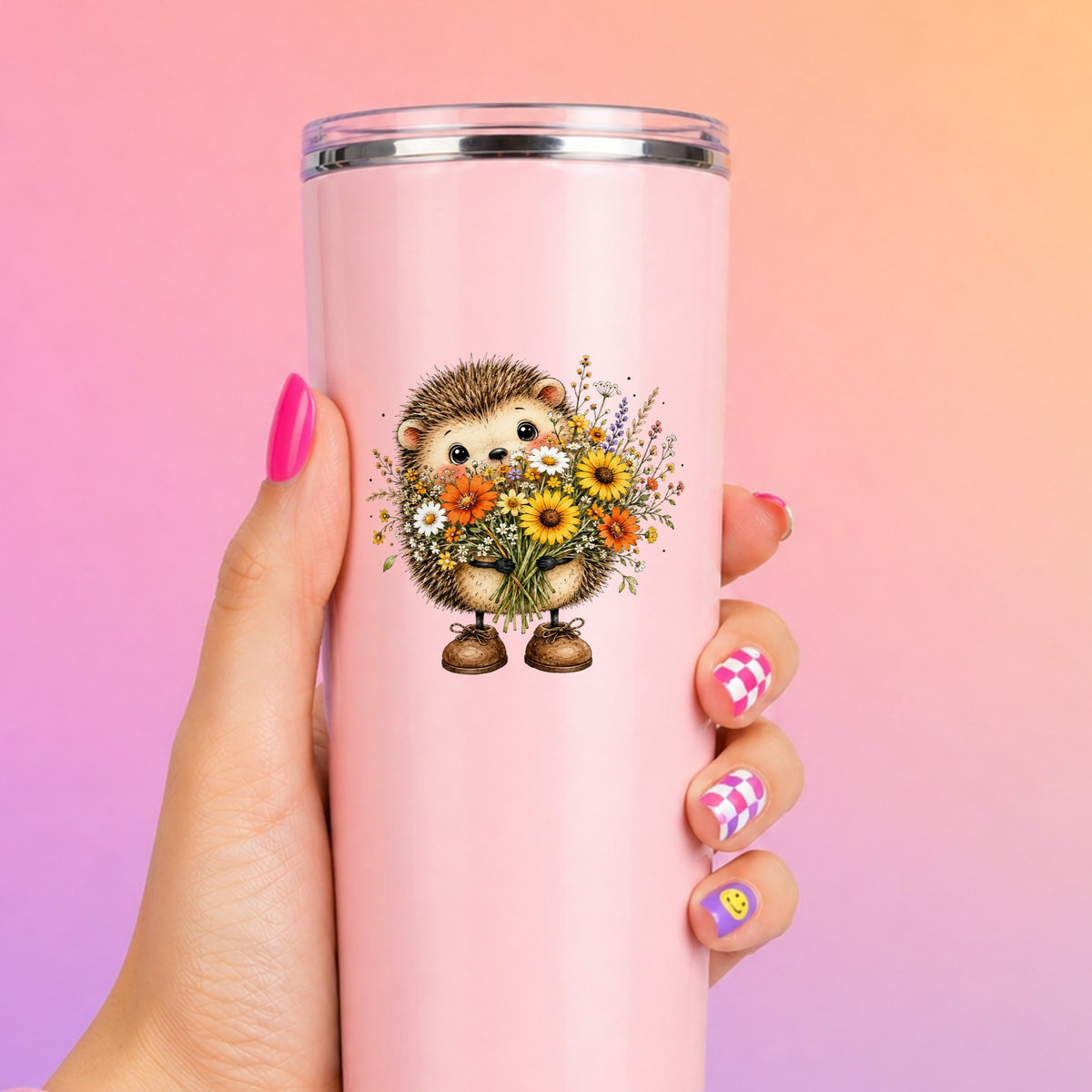 Hedgehog Holding Wildflower Bouquet UV DTF sticker applied to a tall pink tumbler on a pink and orange background