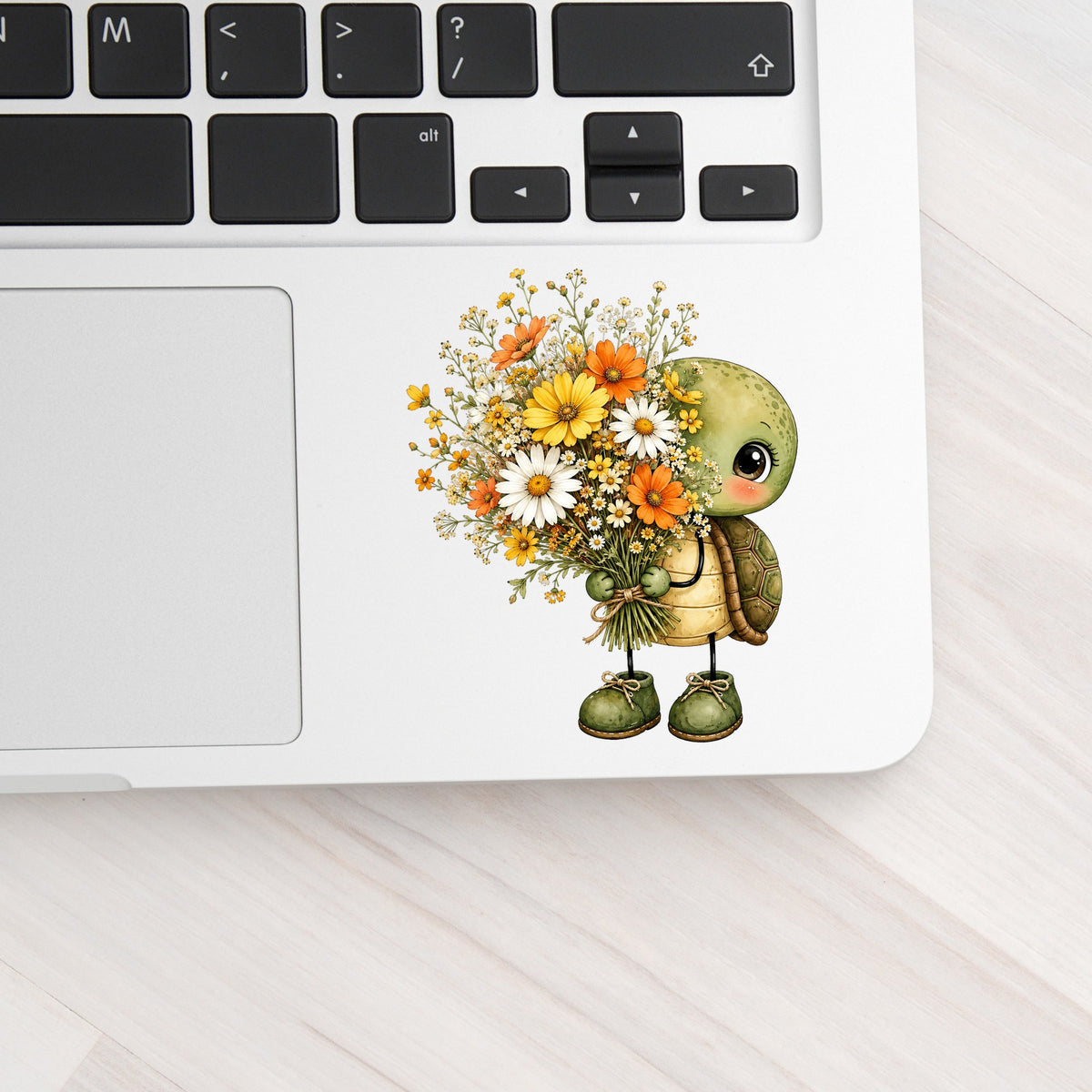 Baby Turtle Holding Wildflower Bouquet UV DTF sticker applied to a silver laptop beside the keyboard