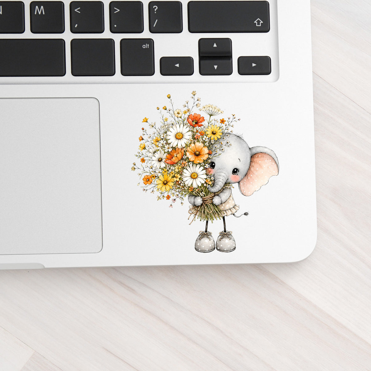 Baby Elephant Holding Daisy Bouquet UV DTF sticker applied to a silver laptop beside the keyboard