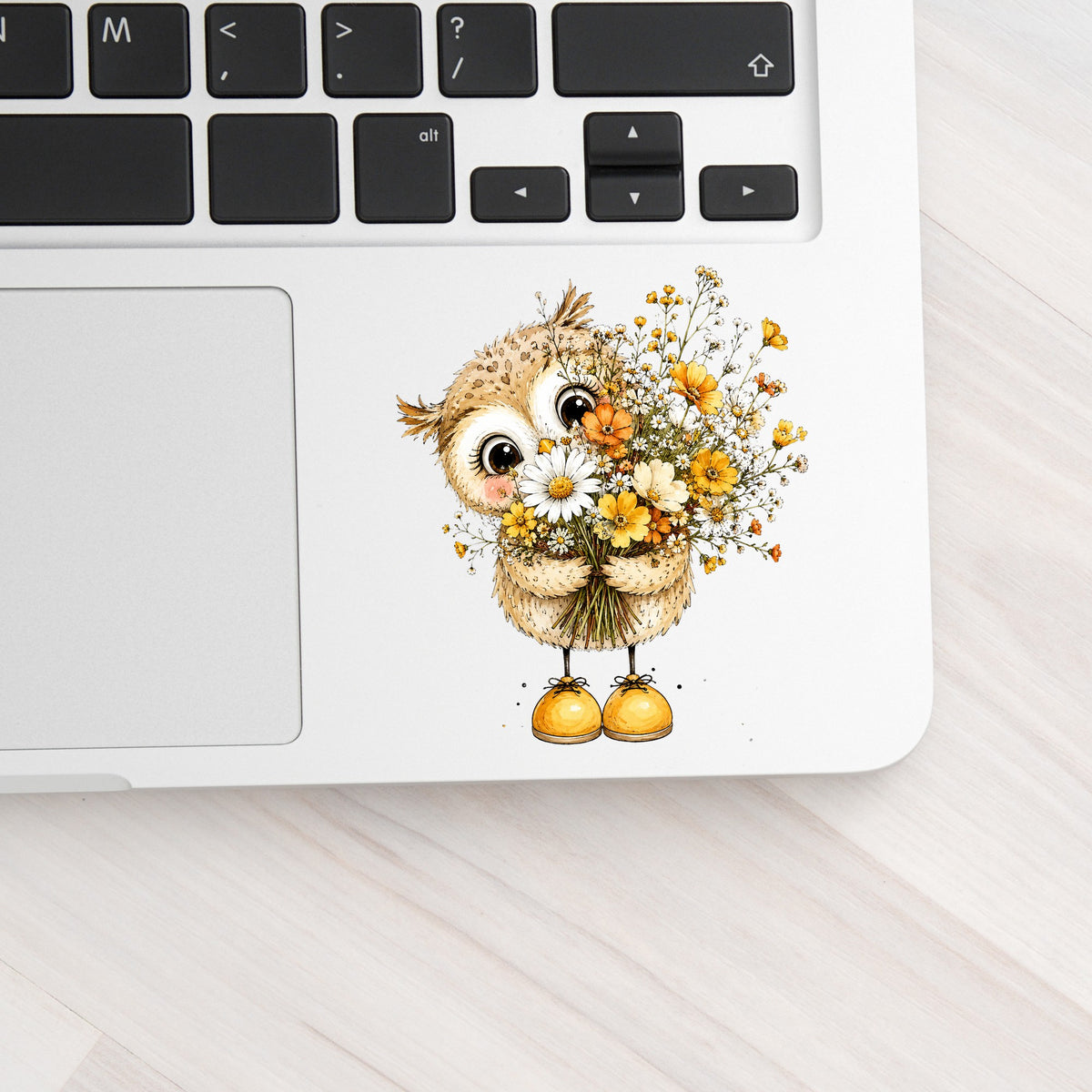 Baby Owl Holding Wildflower Bouquet UV DTF sticker applied to a silver laptop beside the keyboard