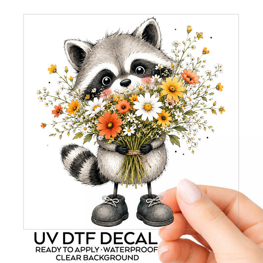 Raccoon Holding Wildflower Bouquet UV DTF sticker on its backing card, held in hand