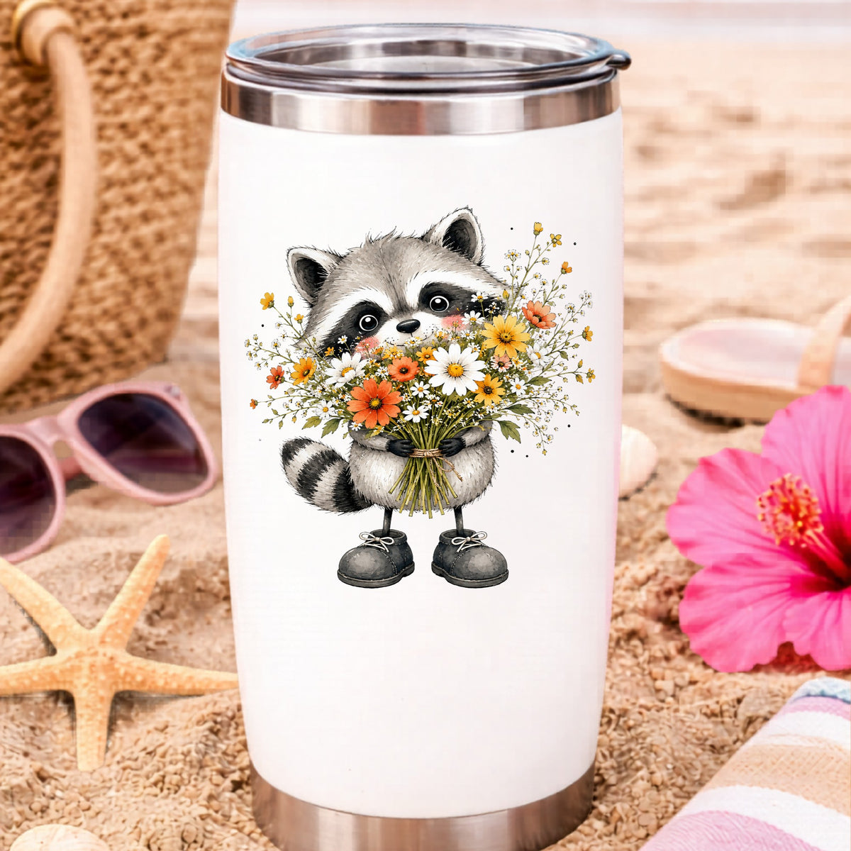 Raccoon Holding Wildflower Bouquet UV DTF sticker applied to a white travel tumbler on beach sand