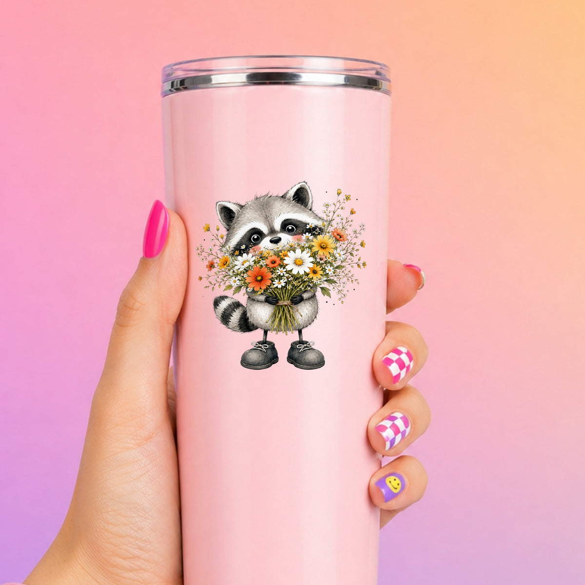 Raccoon Holding Wildflower Bouquet UV DTF sticker applied to a tall pink tumbler on a pink and orange background