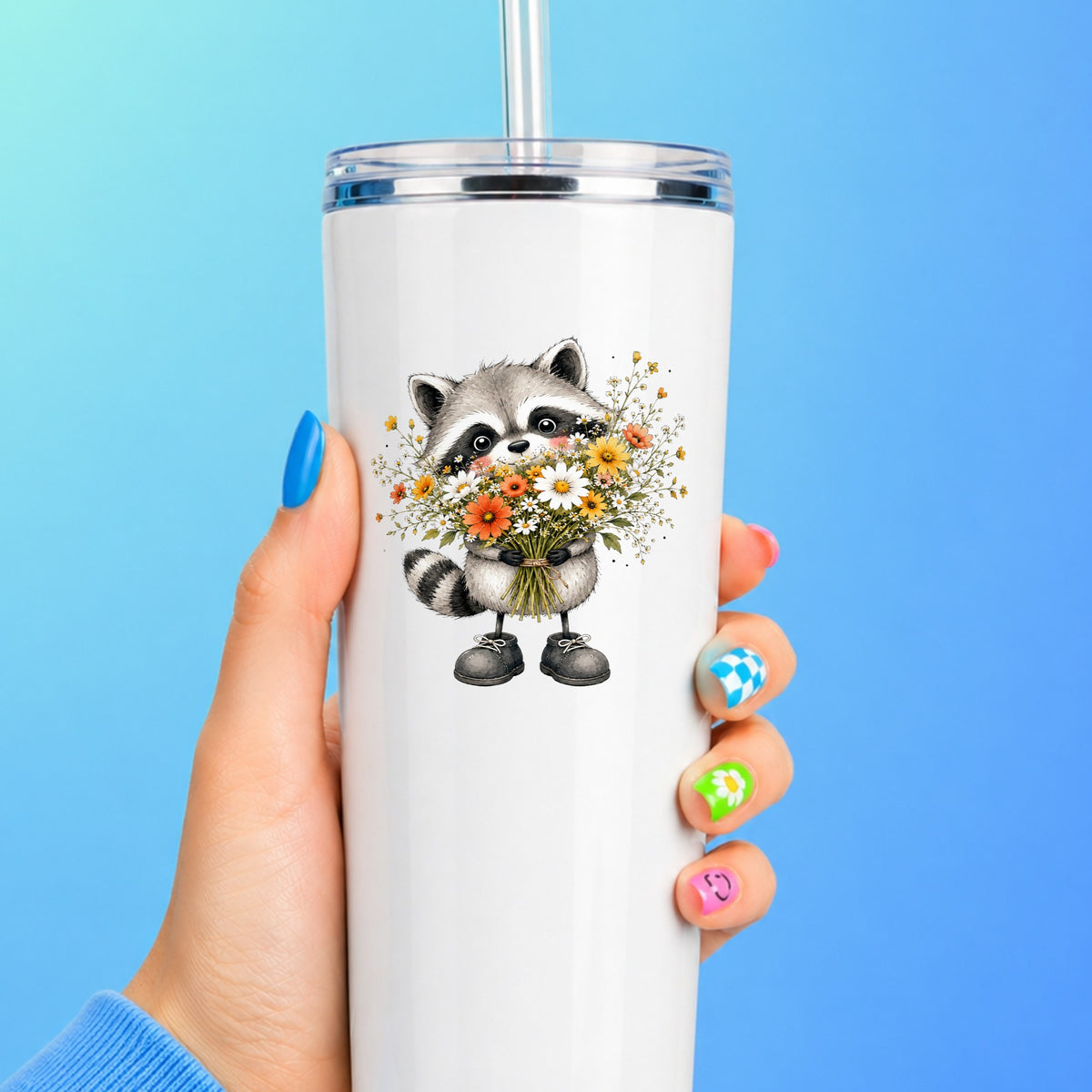 Raccoon Holding Wildflower Bouquet UV DTF sticker applied to a white straw tumbler on a blue background