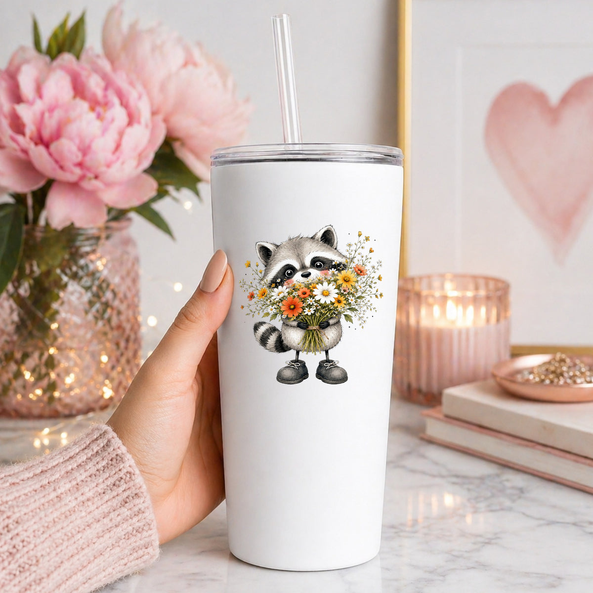 Raccoon Holding Wildflower Bouquet UV DTF sticker applied to a white straw tumbler beside pink peonies