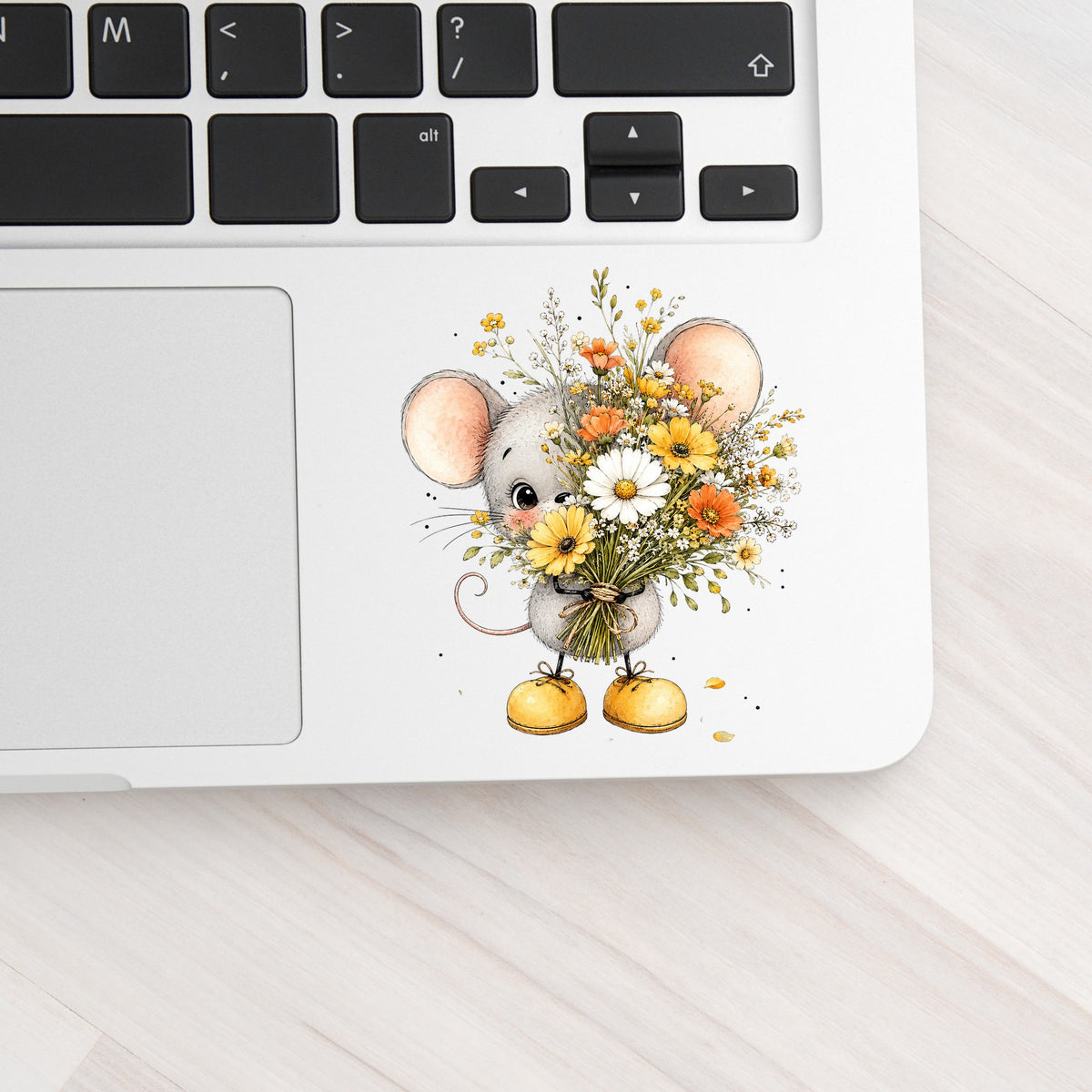 Little Mouse Holding Daisy Bouquet UV DTF sticker applied to a silver laptop beside the keyboard