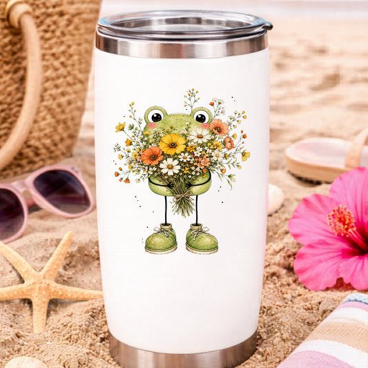 Green Frog Holding Wildflower Bouquet UV DTF sticker applied to a white travel tumbler on beach sand