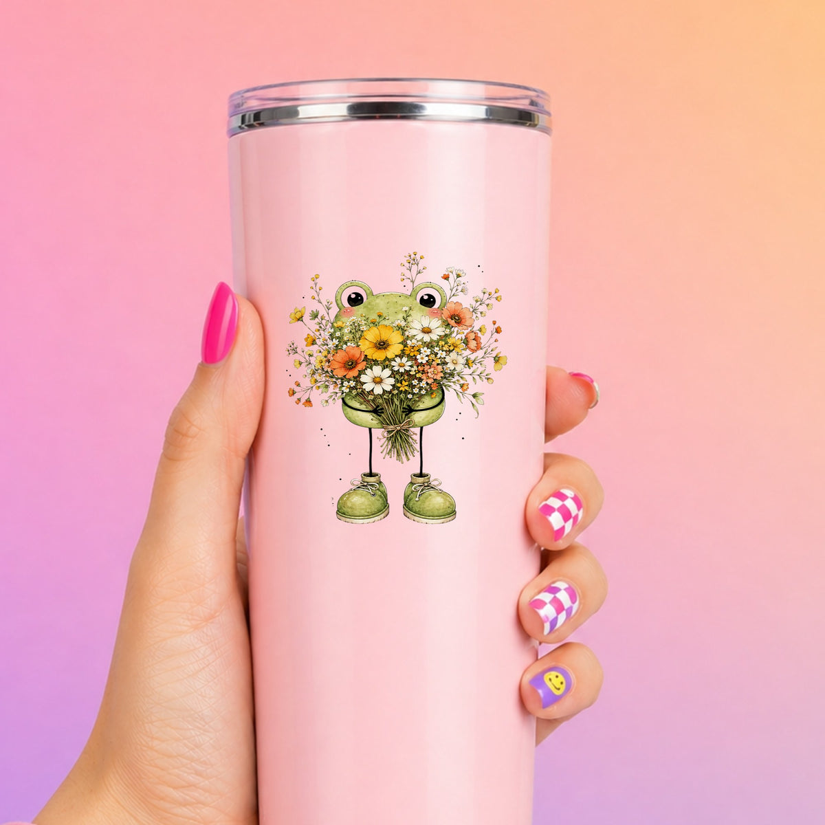 Green Frog Holding Wildflower Bouquet UV DTF sticker applied to a tall pink tumbler on a pink and orange background