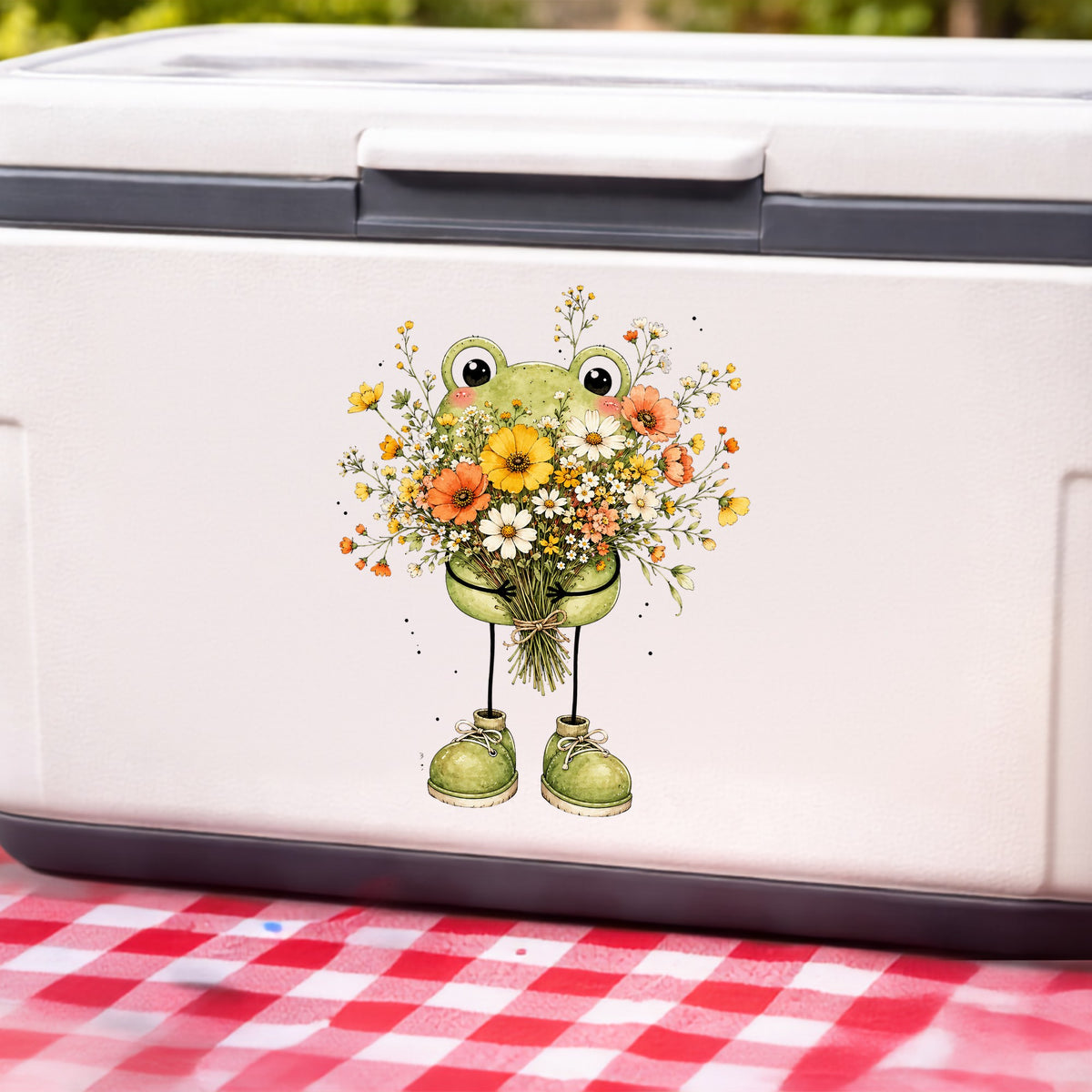Green Frog Holding Wildflower Bouquet UV DTF sticker applied to a white cooler on a red gingham cloth