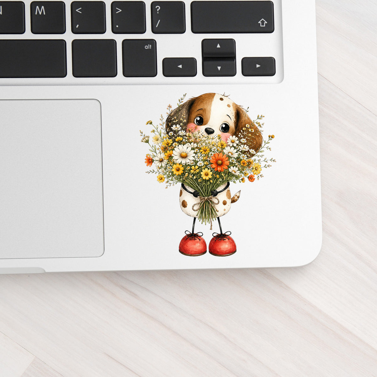 Brown Puppy Holding Daisy Bouquet UV DTF sticker applied to a silver laptop beside the keyboard
