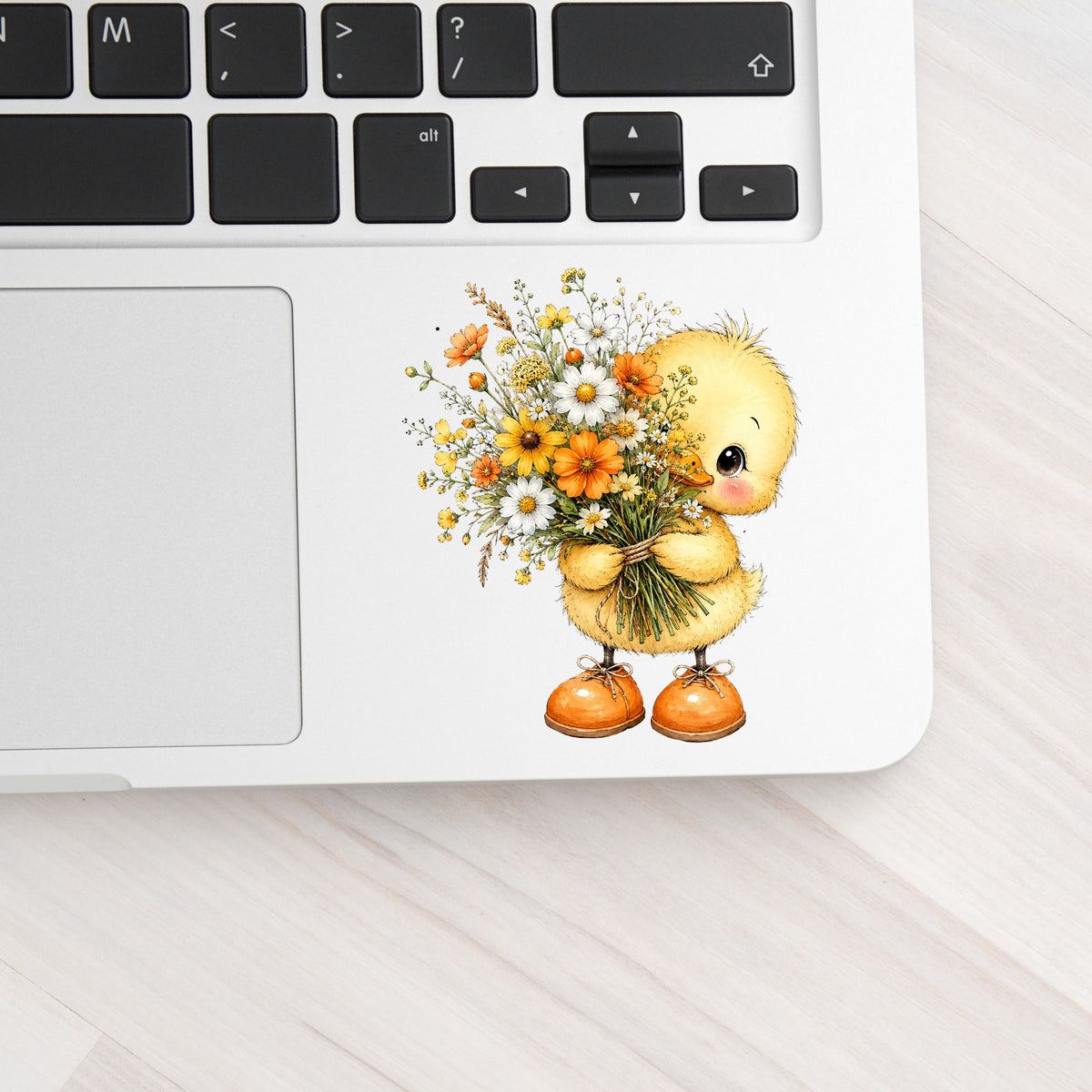 Yellow Duckling Holding Daisy Bouquet UV DTF sticker applied to a silver laptop beside the keyboard
