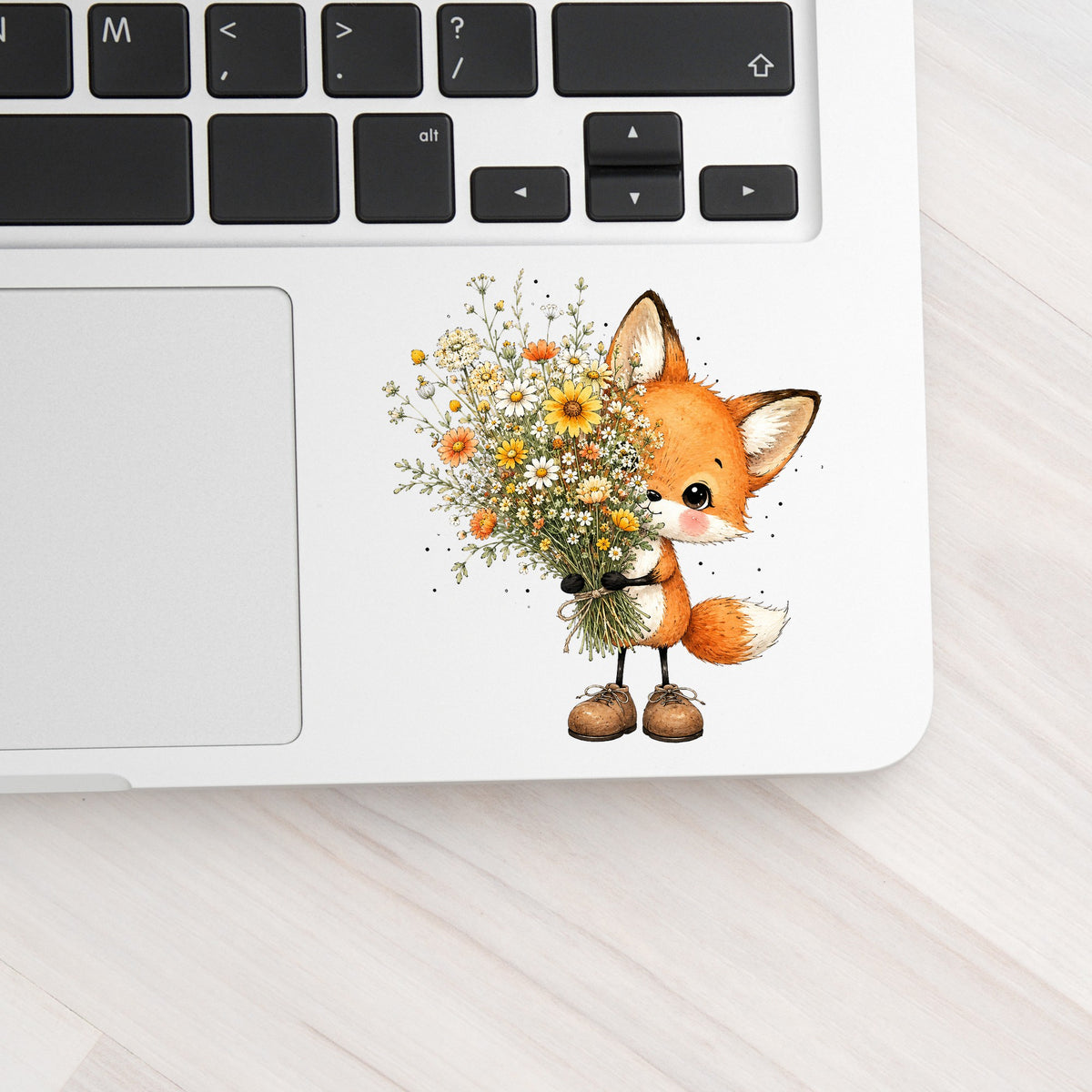 Baby Fox Holding Wildflower Bouquet UV DTF sticker applied to a silver laptop beside the keyboard
