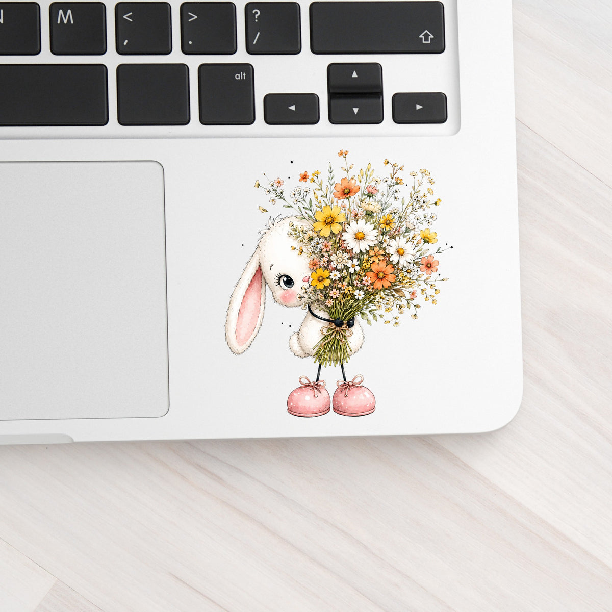 White Bunny Holding Wildflower Bouquet UV DTF sticker applied to a silver laptop beside the keyboard