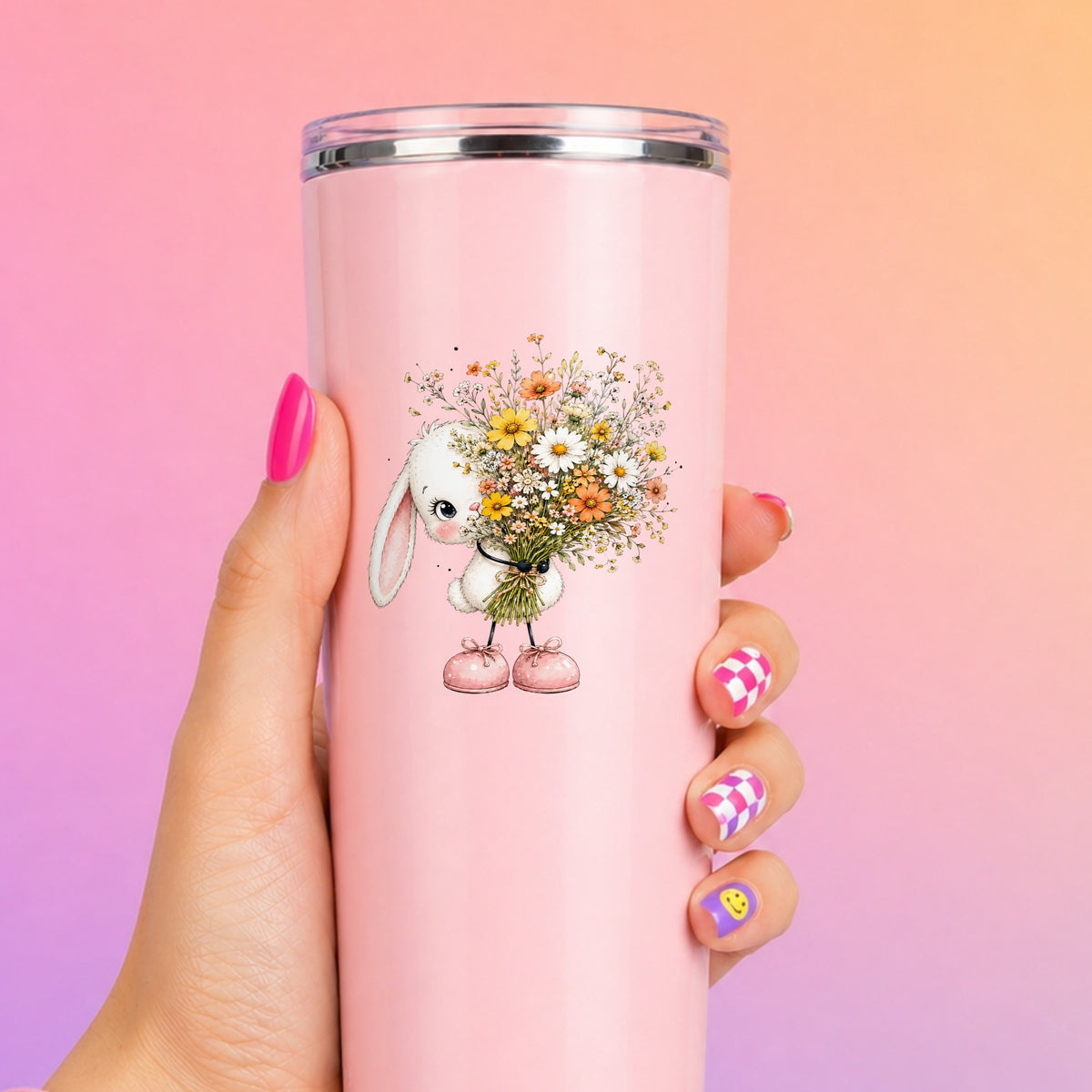 White Bunny Holding Wildflower Bouquet UV DTF sticker applied to a tall pink tumbler on a pink and orange background