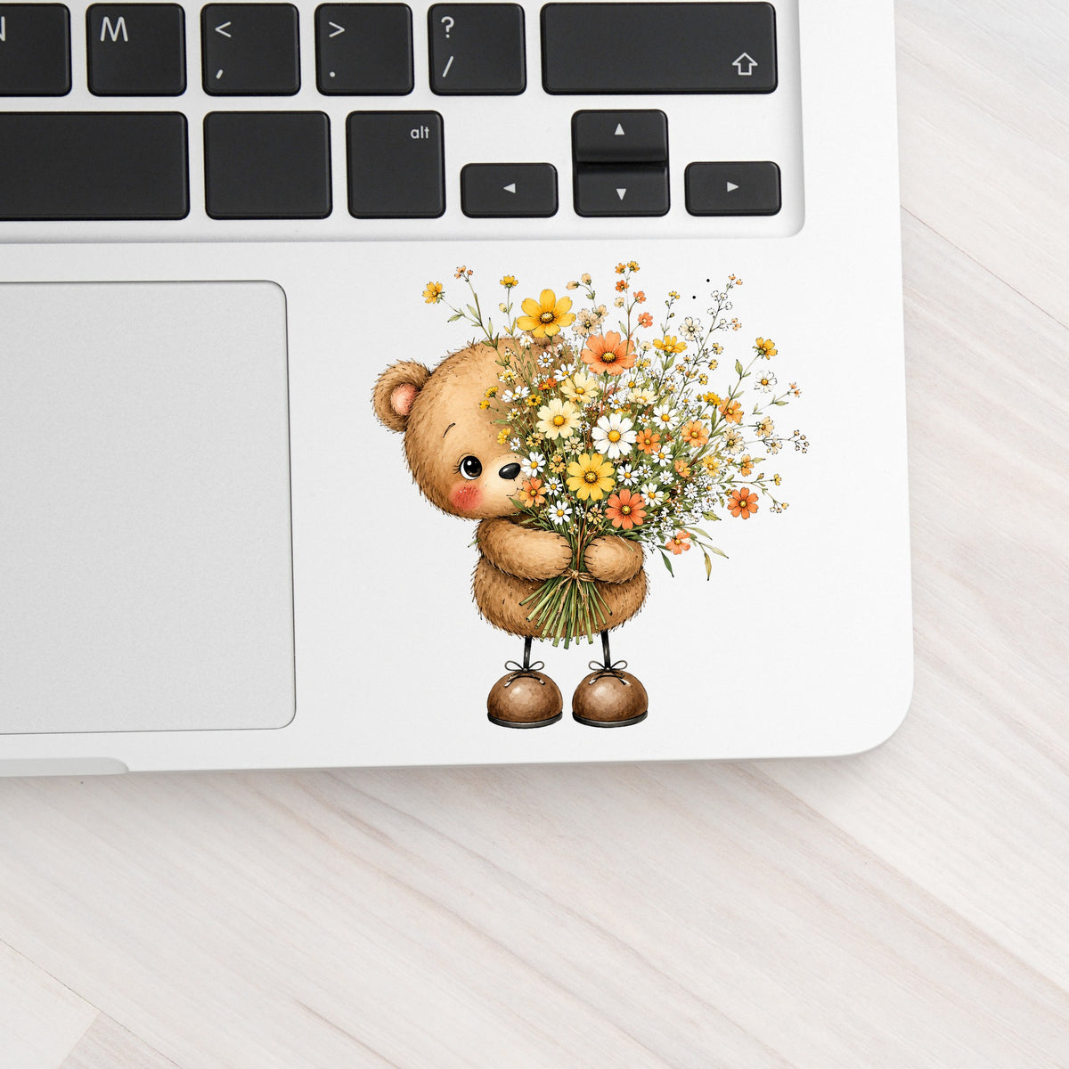 Teddy Bear Holding Wildflower Bouquet UV DTF sticker applied to a silver laptop beside the keyboard