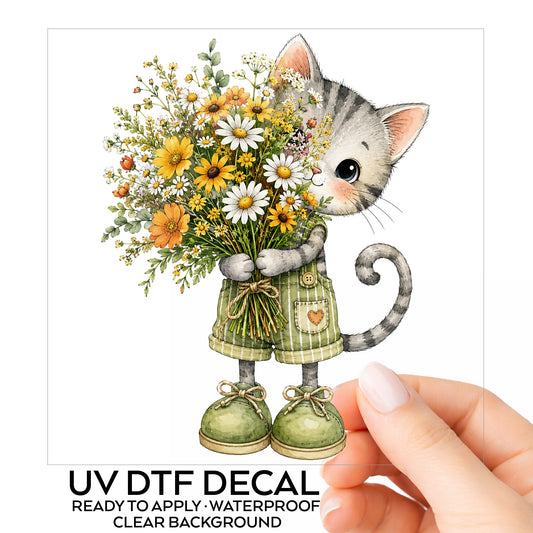 Grey Kitten In Overalls Holding Flowers UV DTF sticker on its backing card, held in hand