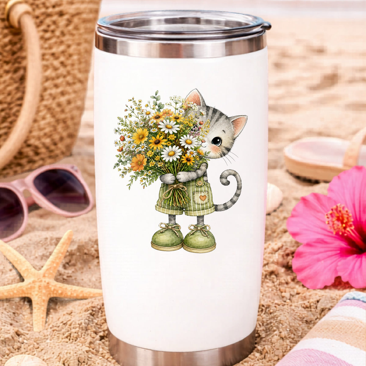 Grey Kitten In Overalls Holding Flowers UV DTF sticker applied to a white travel tumbler on beach sand