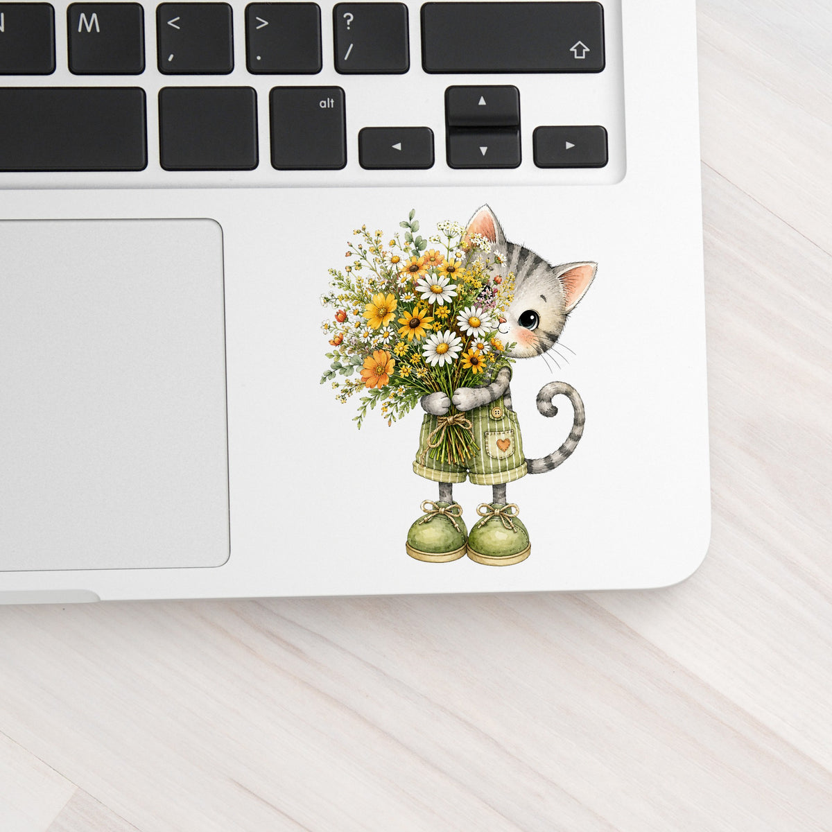 Grey Kitten In Overalls Holding Flowers UV DTF sticker applied to a silver laptop beside the keyboard