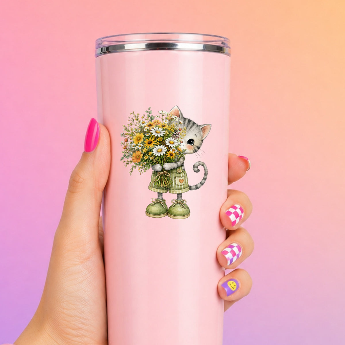 Grey Kitten In Overalls Holding Flowers UV DTF sticker applied to a tall pink tumbler on a pink and orange background