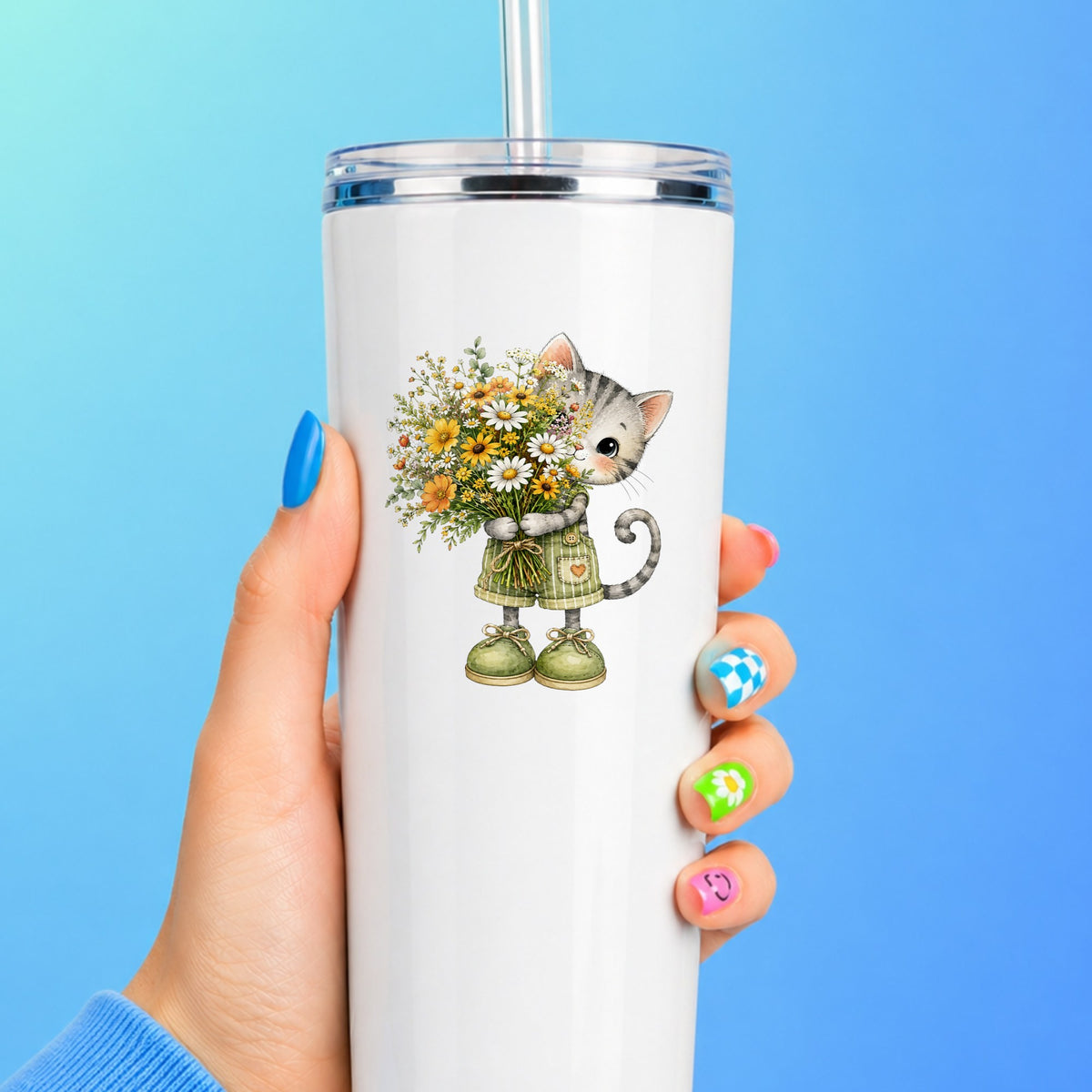 Grey Kitten In Overalls Holding Flowers UV DTF sticker applied to a white straw tumbler on a blue background