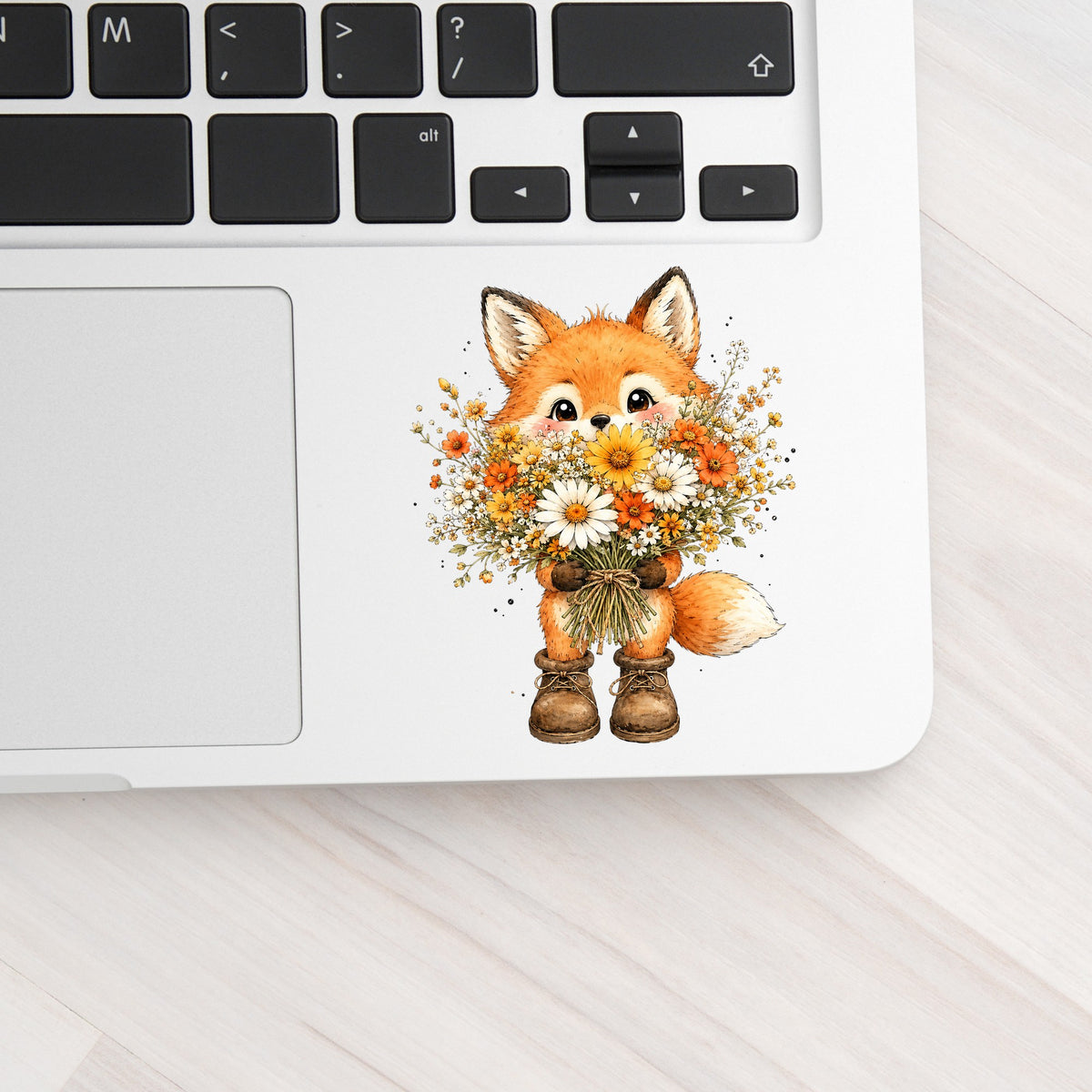 Watercolor Fox Holding Daisy Bouquet UV DTF sticker applied to a silver laptop beside the keyboard