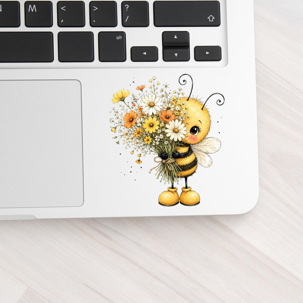 Honey Bee Holding Wildflower Bouquet UV DTF sticker applied to a silver laptop beside the keyboard