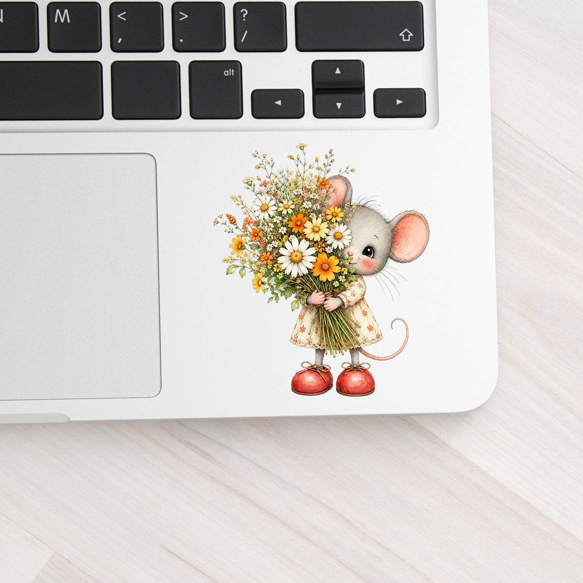 Mouse In Floral Dress Holding Flowers UV DTF sticker applied to a silver laptop beside the keyboard