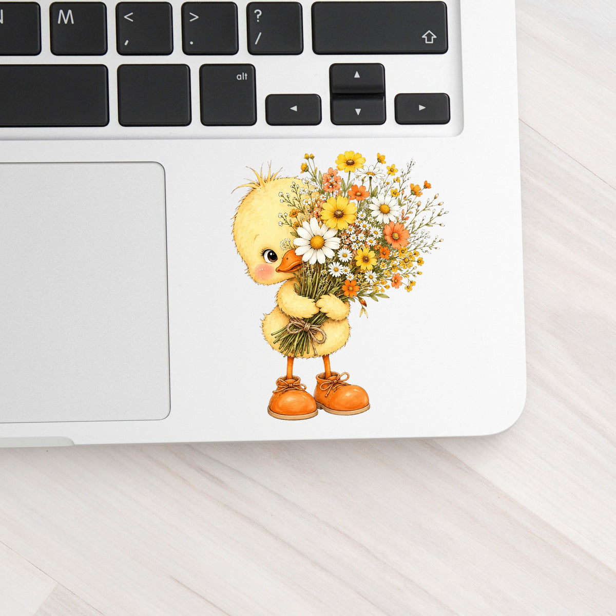 Baby Duck Holding Wildflower Bouquet UV DTF sticker applied to a silver laptop beside the keyboard