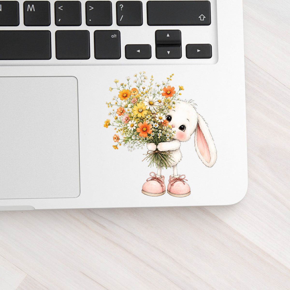 Baby Bunny Holding Daisy Bouquet UV DTF sticker applied to a silver laptop beside the keyboard