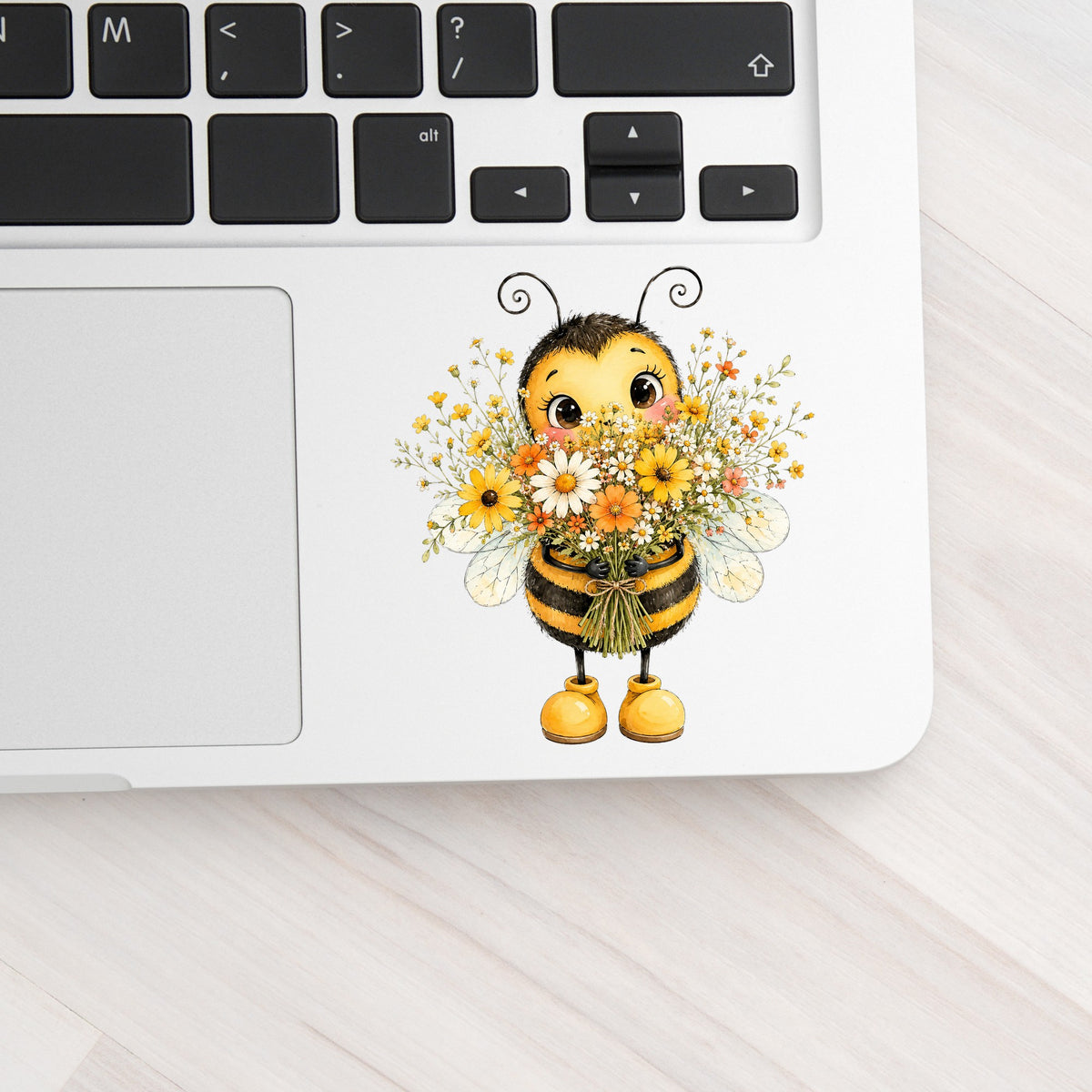 Bumble Bee Holding Daisy Bouquet UV DTF sticker applied to a silver laptop beside the keyboard
