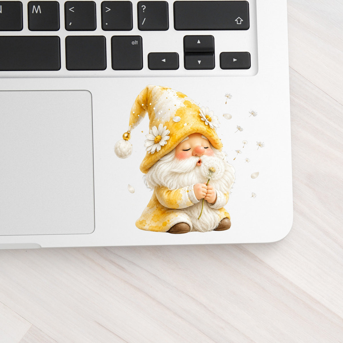 Gnome Blowing A Dandelion UV DTF sticker applied to a silver laptop beside the keyboard