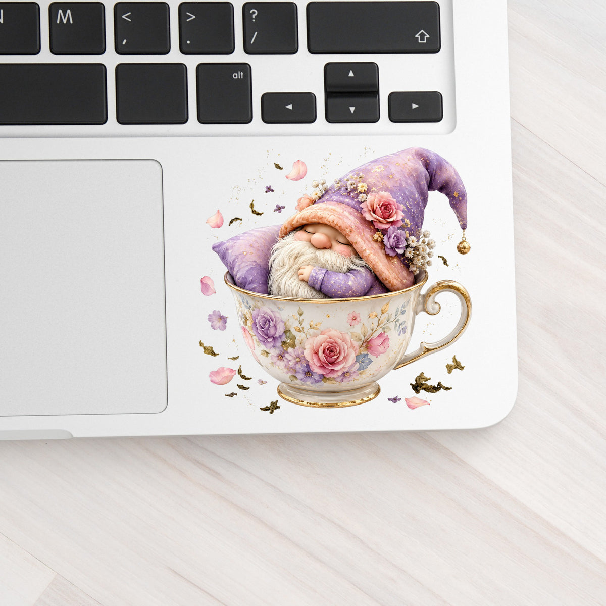 Gnome Sleeping In Teacup UV DTF sticker applied to a silver laptop beside the keyboard