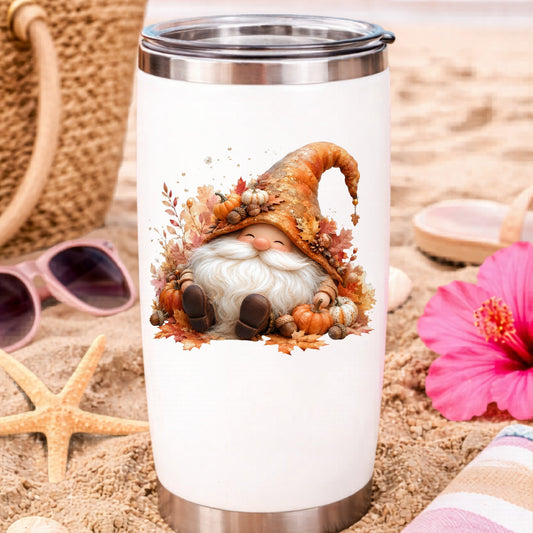 Autumn Gnome With Pumpkins UV DTF sticker applied to a white travel tumbler on beach sand