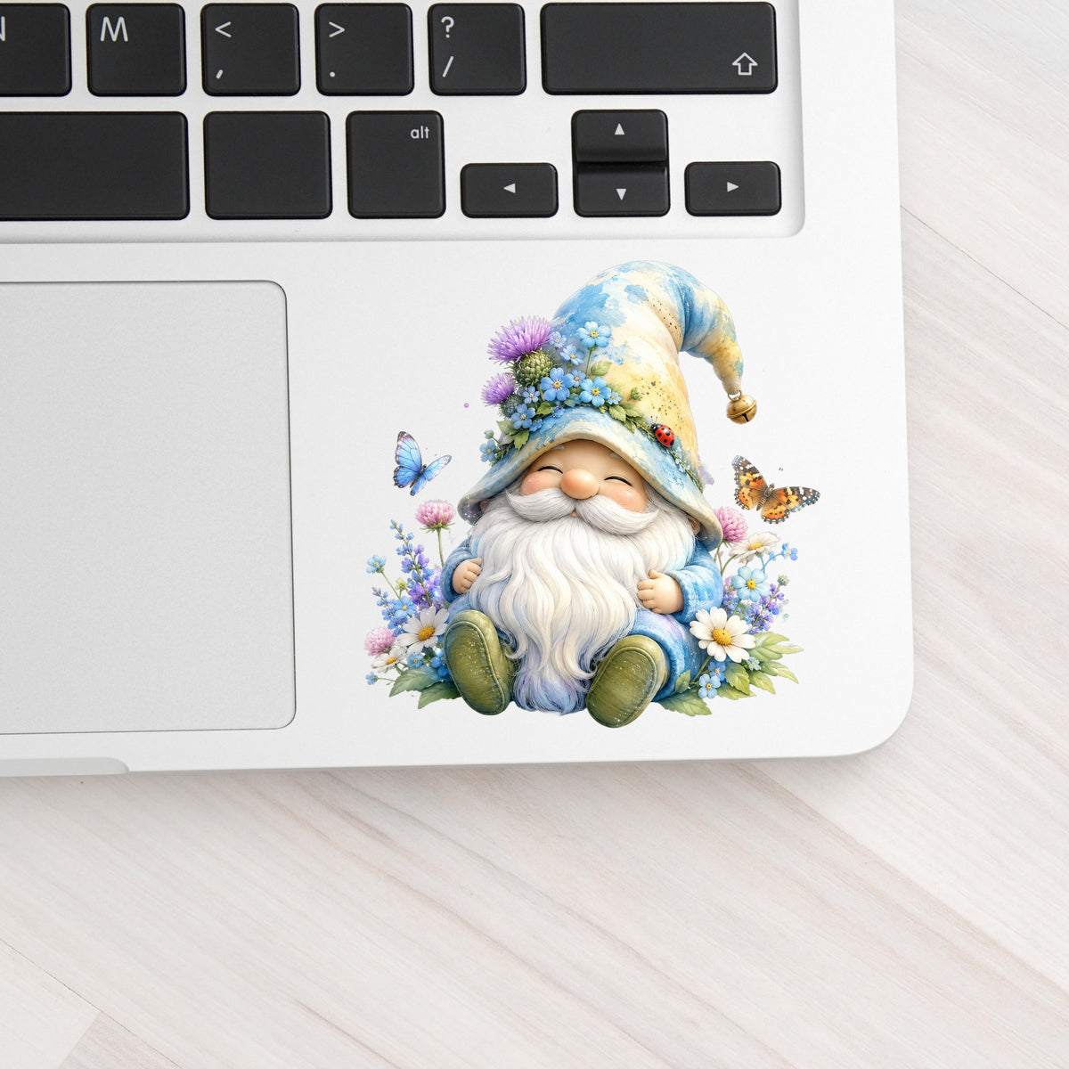 Wildflower Gnome With Butterflies UV DTF sticker applied to a silver laptop beside the keyboard