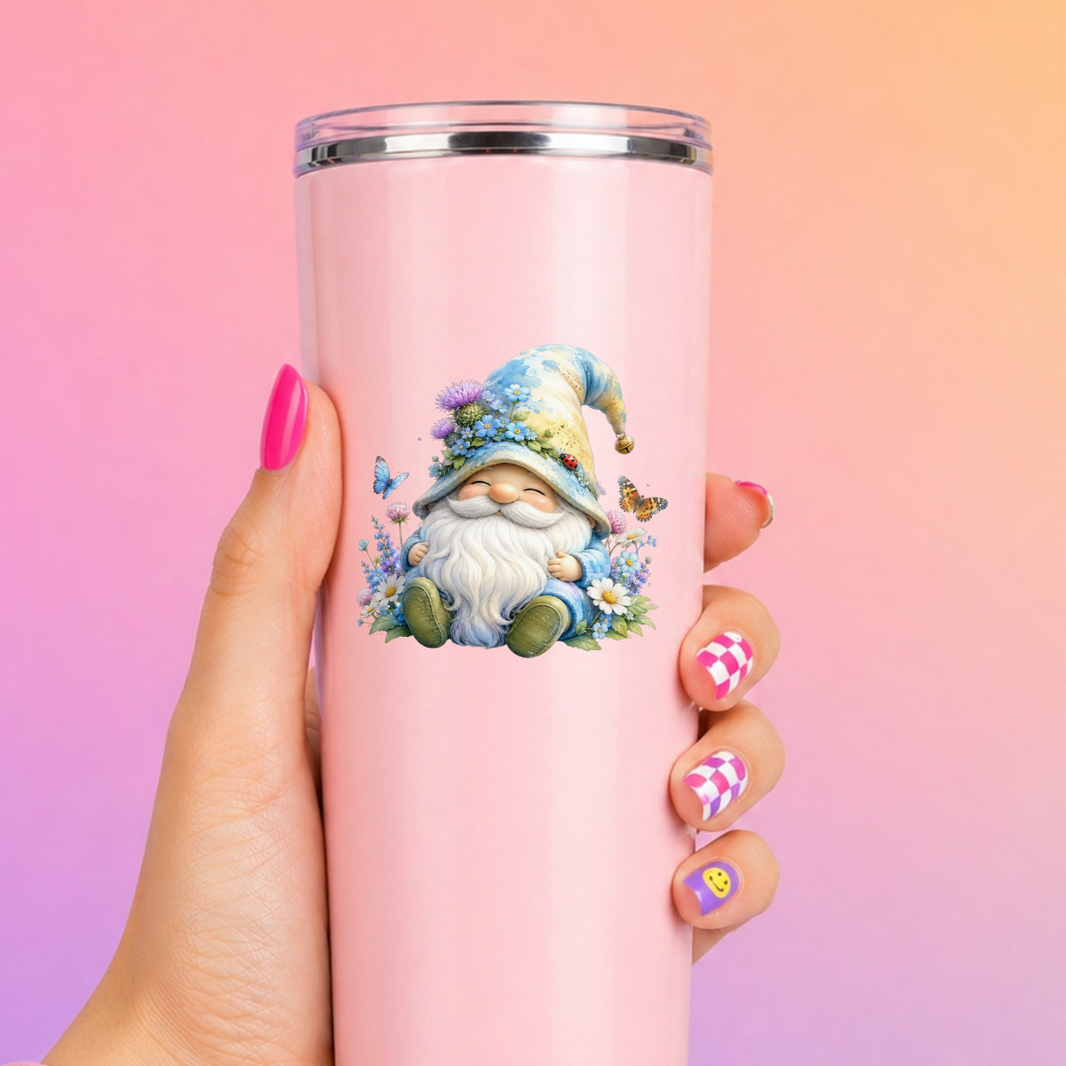 Wildflower Gnome With Butterflies UV DTF sticker applied to a tall pink tumbler on a pink and orange background