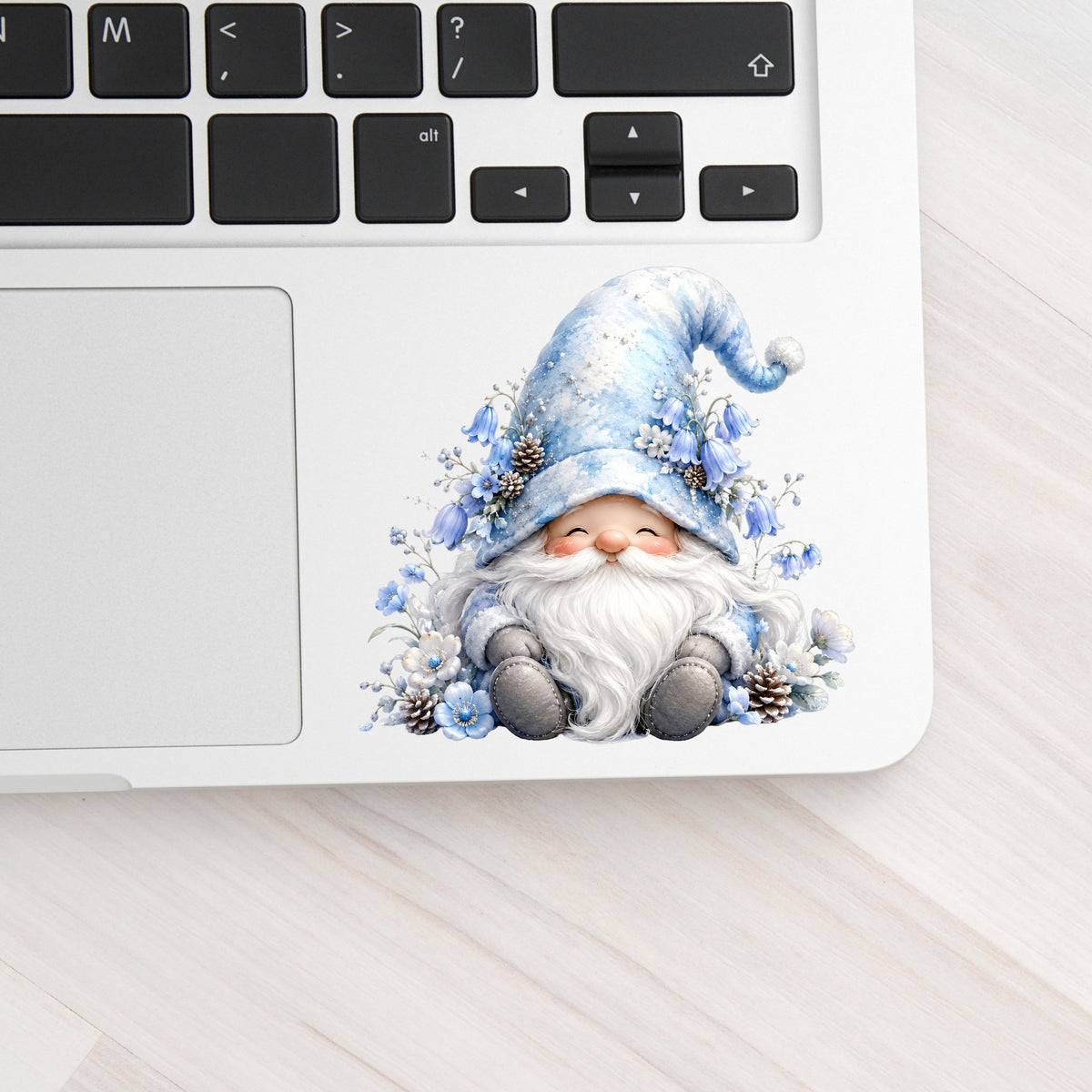 Winter Gnome With Pinecones UV DTF sticker applied to a silver laptop beside the keyboard