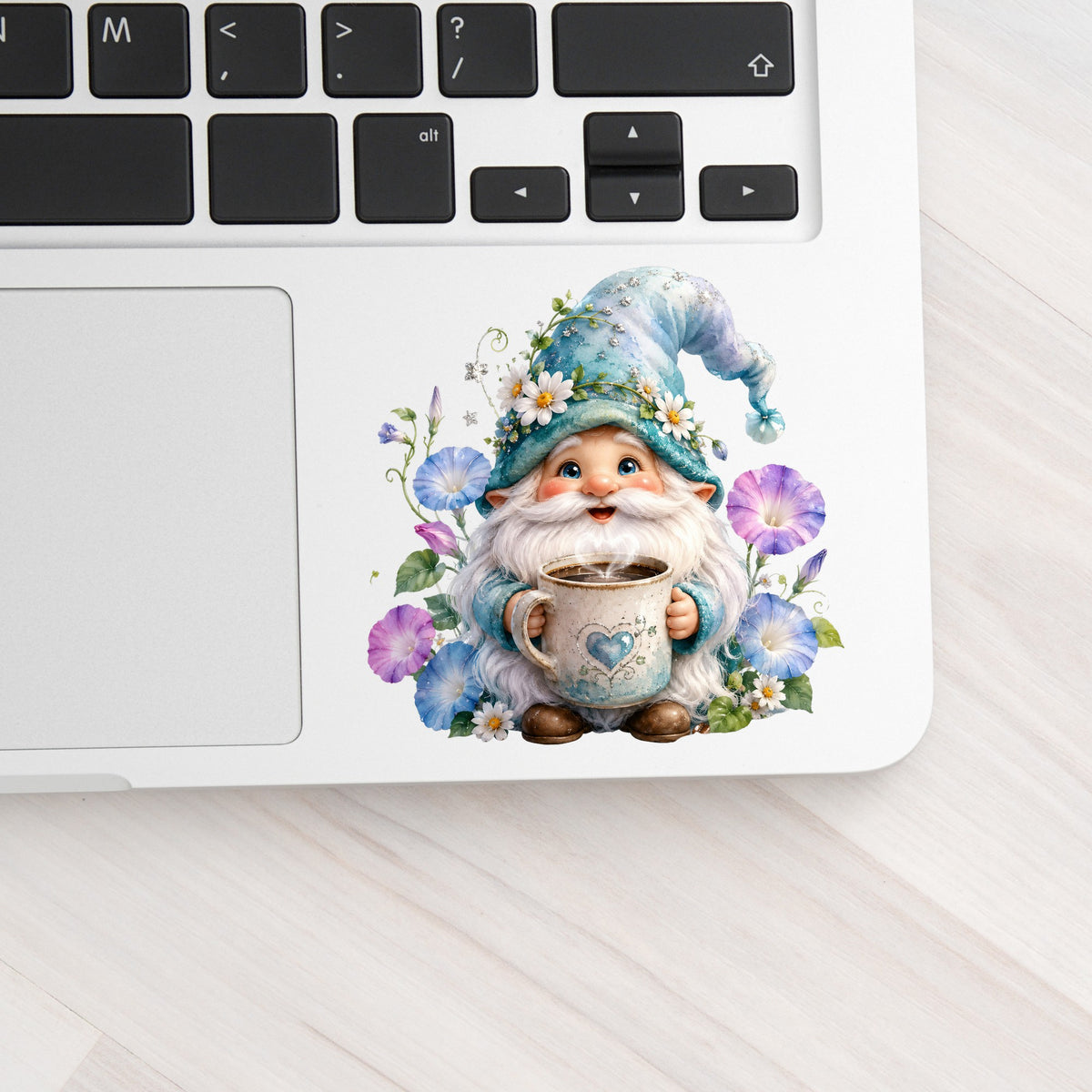 Gnome Holding Coffee Mug UV DTF sticker applied to a silver laptop beside the keyboard