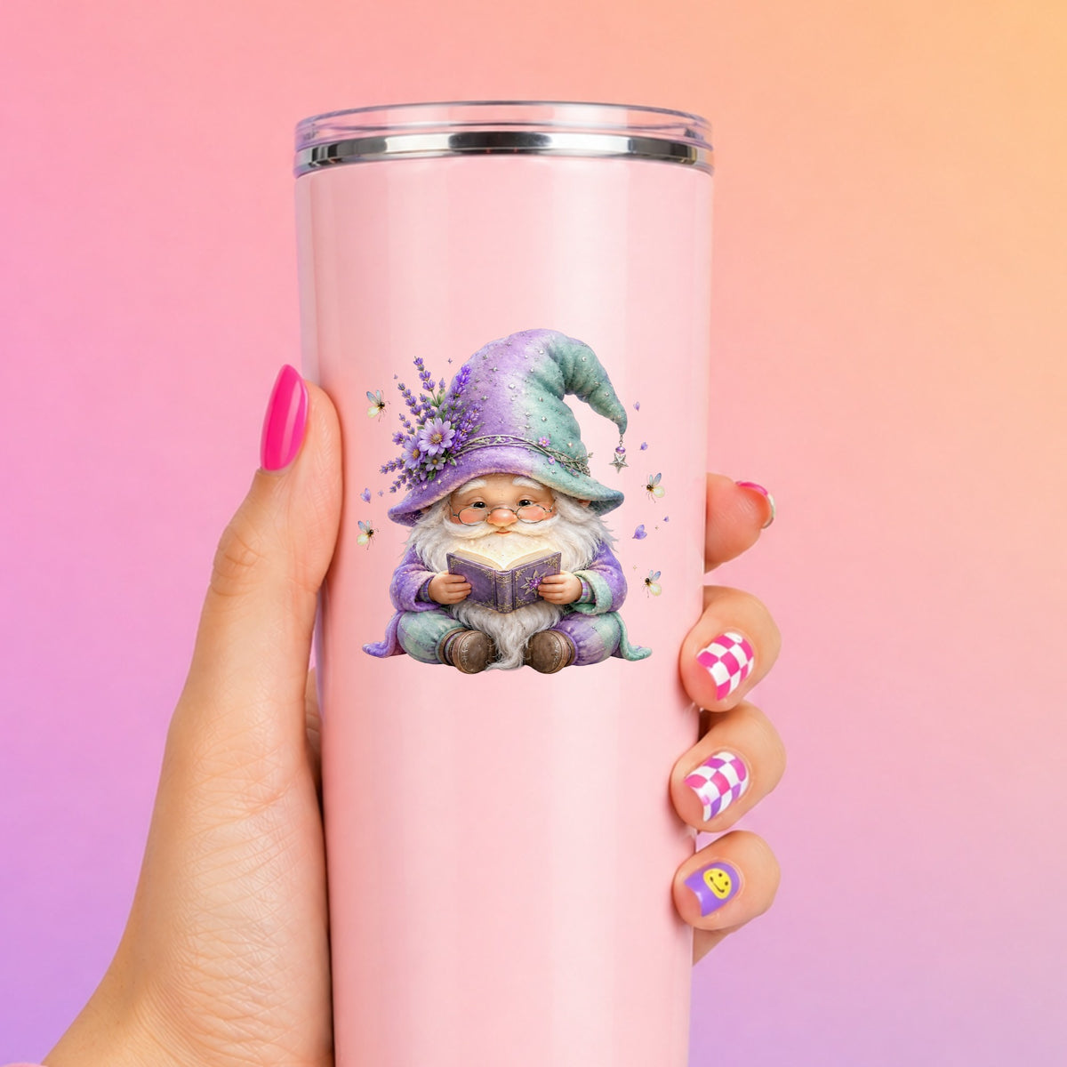 Lavender Reading Gnome With Fireflies UV DTF sticker applied to a tall pink tumbler on a pink and orange background