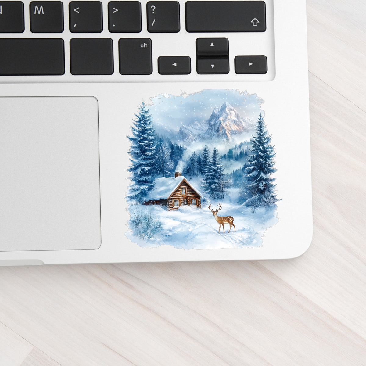 Blue Winter Cabin With Deer UV DTF sticker applied to a laptop beside the keyboard