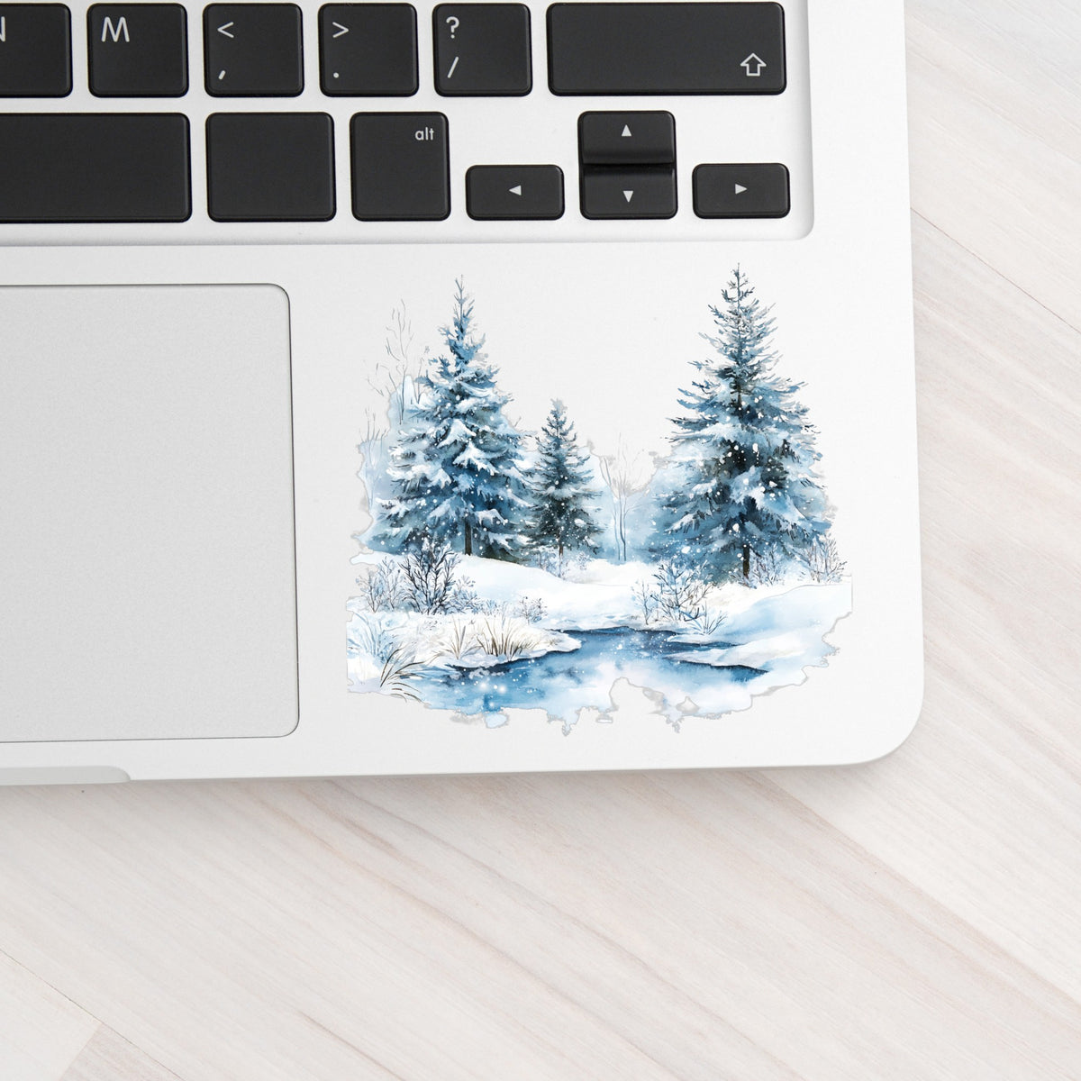Snowy Evergreens By Stream UV DTF sticker applied to a laptop beside the keyboard