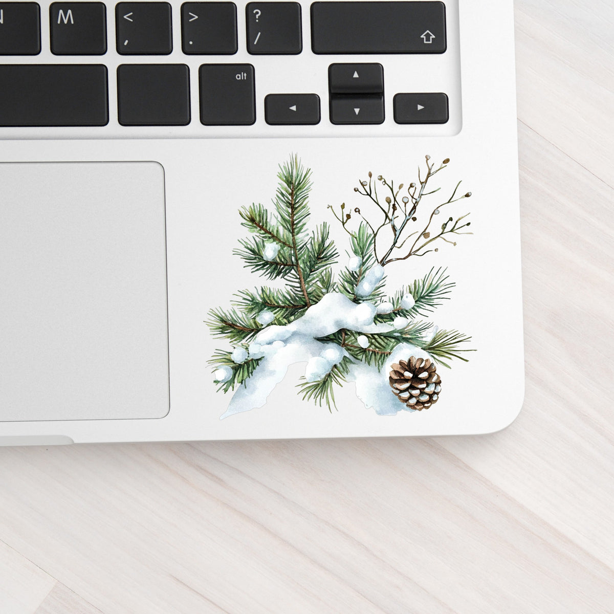 Snowy Pine Branch With Pine Cone UV DTF sticker applied to a laptop beside the keyboard