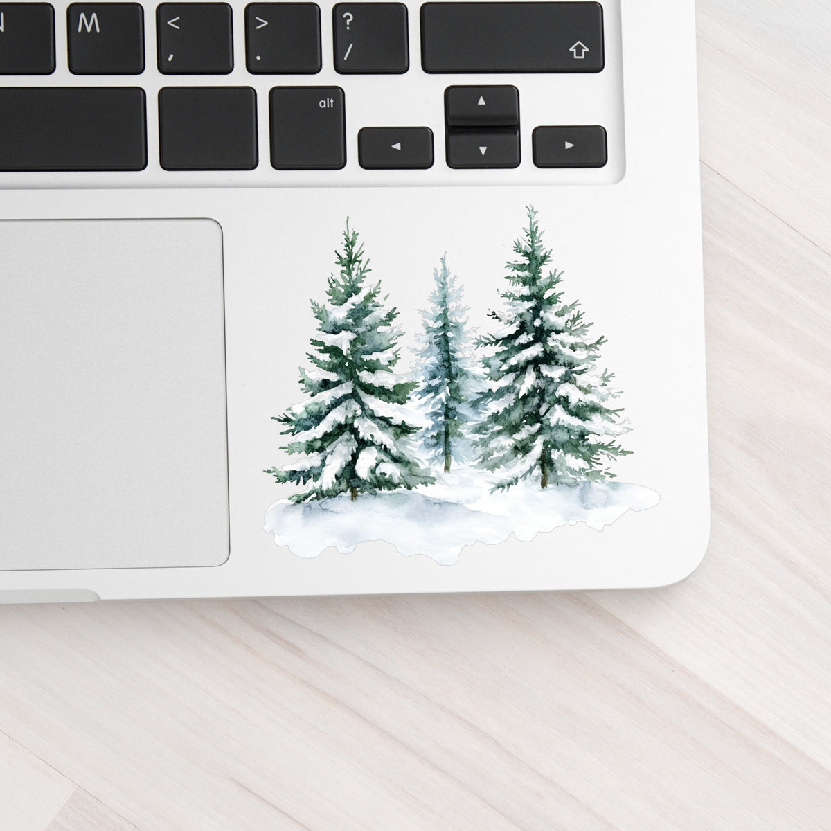 Three Snowy Pine Trees UV DTF sticker applied to a laptop beside the keyboard