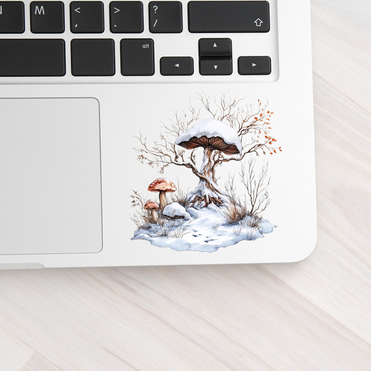 Whimsical Snowy Tree With Mushroom UV DTF sticker applied to a laptop beside the keyboard