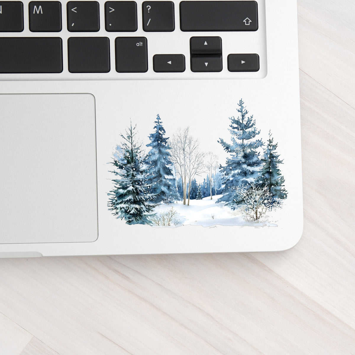 Blue Winter Pines And Birch UV DTF sticker applied to a laptop beside the keyboard