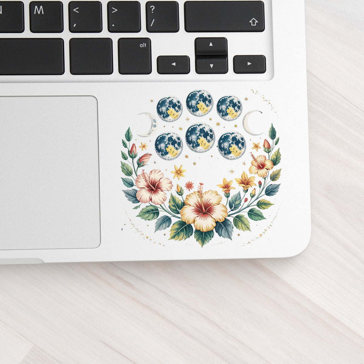 Moon Phases With Hibiscus Flowers UV DTF sticker applied to a silver laptop beside the keyboard