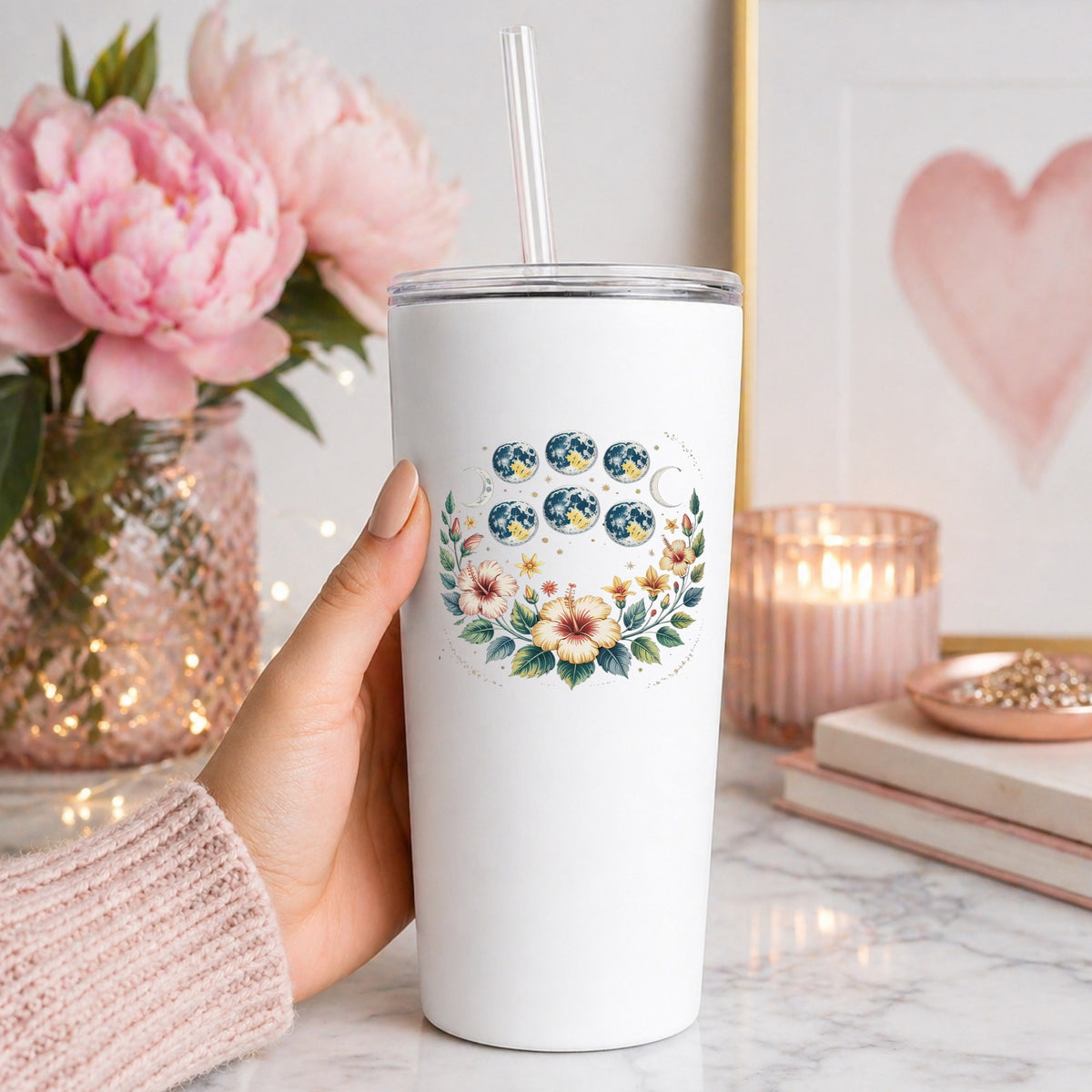 Moon Phases With Hibiscus Flowers UV DTF sticker applied to a white straw tumbler beside pink peonies