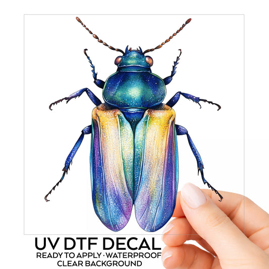 Gold And Blue Jewel Beetle UV DTF sticker on its backing card, held in hand