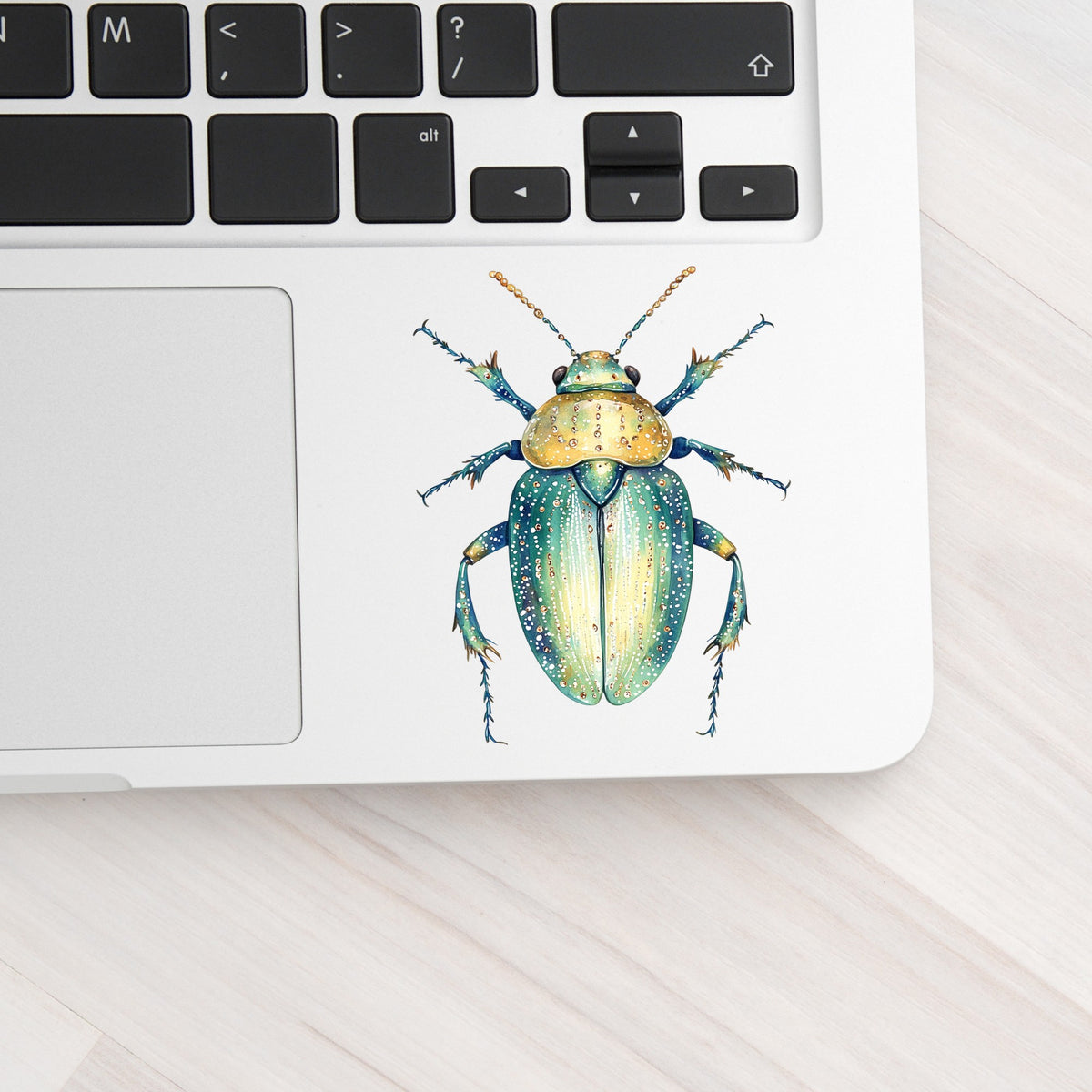 White Dotted Teal Beetle UV DTF sticker applied to a silver laptop beside the keyboard
