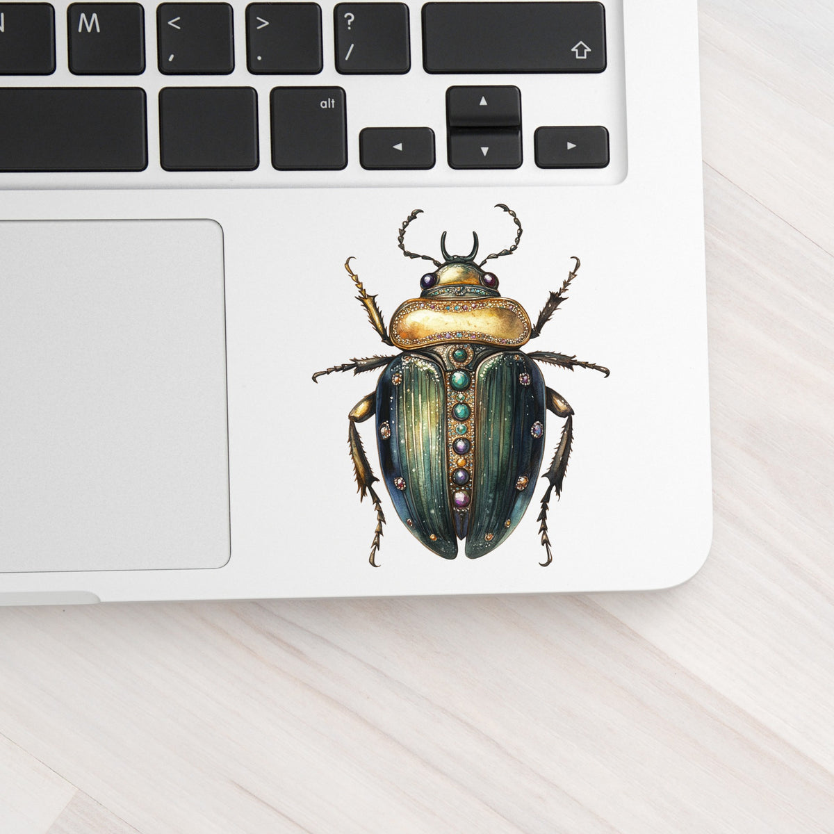 Jeweled Gold Scarab Beetle UV DTF sticker applied to a silver laptop beside the keyboard